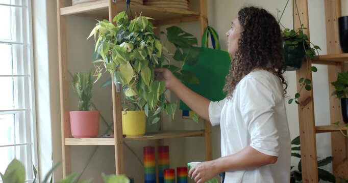 Nonbinary AfricanAmerican entering right misting, caring for plant with spray at window, copy space