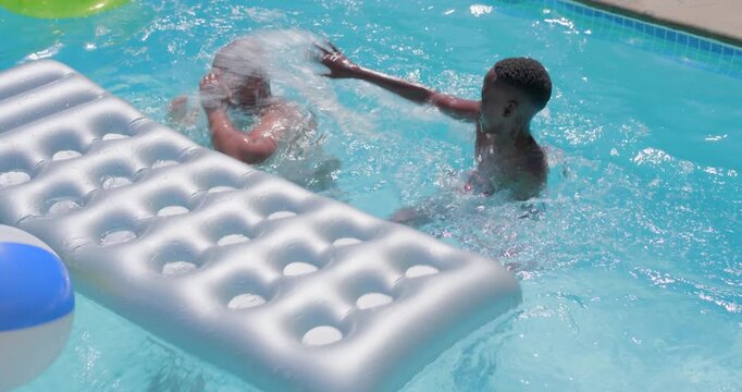 Splashing dad in green trunks and red-trunked son pushing silver float and ball yard pool playfully