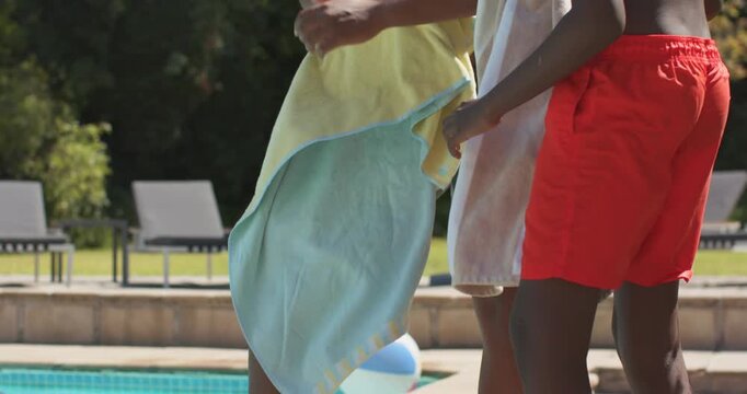 African American father and son drying towels at pool edge after swimming, adult in striped trunks