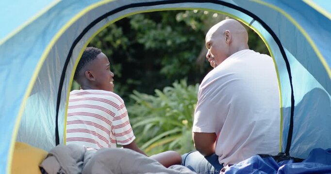 African father and son in pop-up tent, father gesturing and reaching, child clasping hands, playing