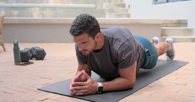 Man starting plank on patio mat shifting, rolling to seated stretching with weights for cooldown