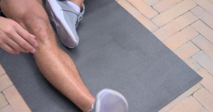 Noticing loose laces, man pulling toes and adjusting gray sneaker on patio mat, warming up