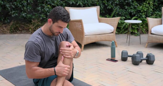 Male is starting cross-legged, pulling knee to chest and massaging shin on patio mat for mobility