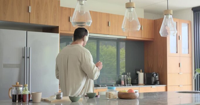 After phone buzzing man is checking screen while wearing headphones and eating cereal near fridge