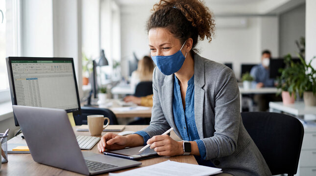 Young woman working on laptop while wearing mask in modern office  