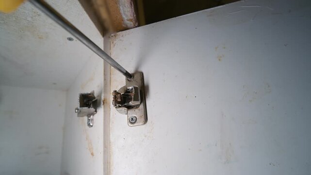 Screwdriver Removing Screw from Broken Cabinet Door Hinge | Damaged Silumin Kitchen Furniture Hardware Disassembly Close-Up | Home Repair and Renovation