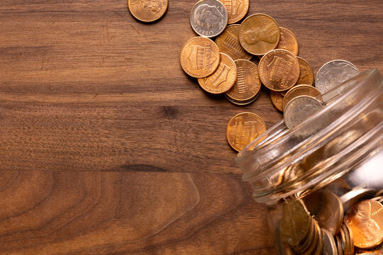 Top-Down View of Coins Spilling from Glass Jar onto Wooden Surface
