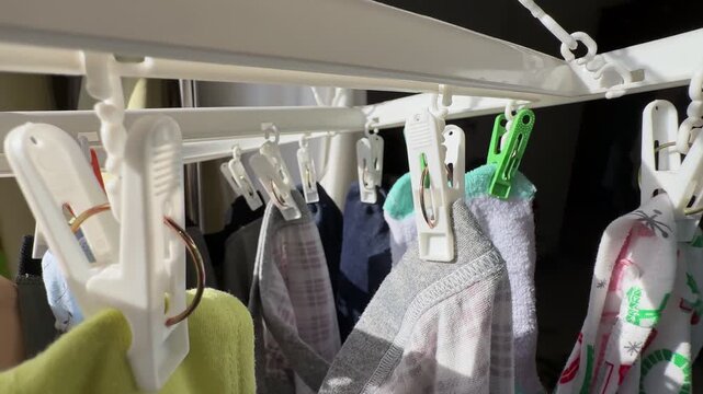 Close-up of socks and small garments clipped to an indoor drying rack by a sunlit window, showing everyday household laundry care, fabric texture, and natural daylight at home.