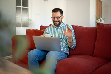 Obraz premium Smiling man waving during remote video conference at home