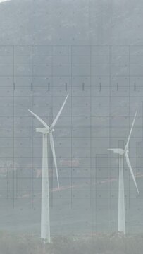 Vertical video: Two wind turbines rotating on hill wind turning blades for power fixed grid visible