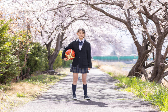 桜の下でバスケットボールを持つ新一年生