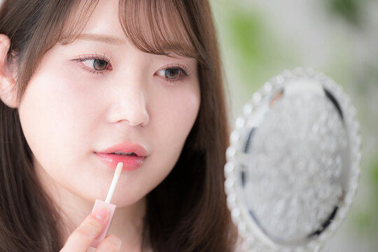 手鏡を見ながらリップを塗る女性のナチュラルメイクと美容ケア　リップグロスや唇のケアなどのイメージクローズアップ