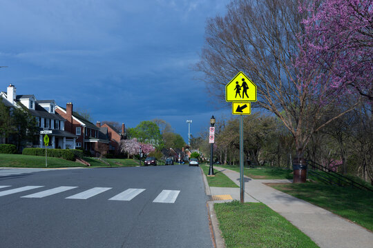 Residential neighborhood in Frederick, Maryland, with yellow school crossing sign and pink spring blossoms under a dark storm sky on S Jefferson Street.