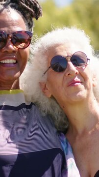 Vertical video: Entering left, senior wrapping arm around friend at park, posing with striped top