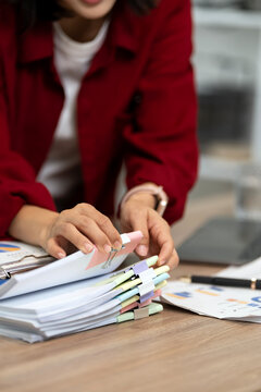 Close up of a professional woman in red shirt organizing office documents and paperwork on wooden desk, business lifestyle concept.