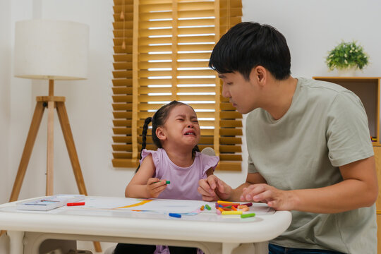 father comforting crying preschool child girl while drawing and painting with oil pastels at