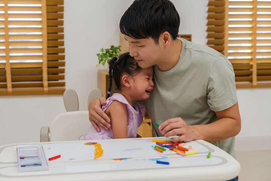 father comforting crying preschool child girl while drawing and painting with oil pastels at