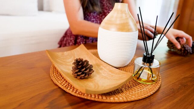 Asian Woman Arranging Pine Cones Near Essential Oil Diffuser on Table