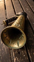 Fototapeta premium Antique brass maritime megaphone rests on a weathered wooden surface.