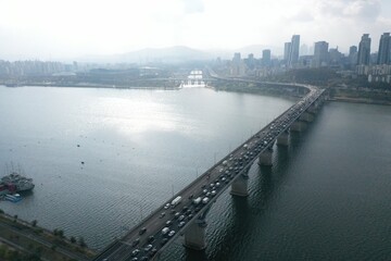 Obraz premium Aerial shot of a long bridge stretching across a wide river with urban surroundings.