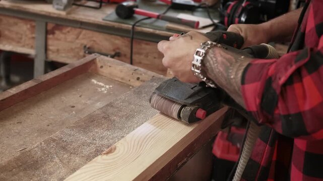 Sanding wood. Carpentry tool. Male joiner hand smoothing new plank surface with professional belt sander equipment rubbing material.