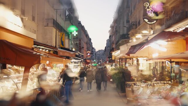 People walking down busy market street in paris at dusk