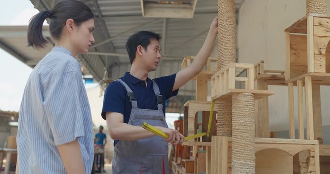 Entrepreneur and carpenter review wooden furniture mockup and prototype pieces, discuss design details and inspect quality at a small business workshop during product development.
