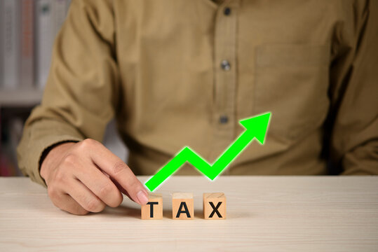 Man holding wooden blocks with tax word and green upward arrow. Concept of tax increase, rising corporate tax rate, economic inflation, financial burden, government policy and accounting cost.