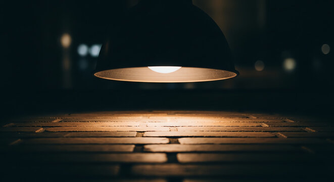 A hanging lamp casts a warm subtle glow on a brick surface in a dark room.