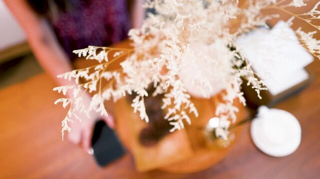 Woman Placing Smartphone on Wooden Cafe Table with Dried Flowers