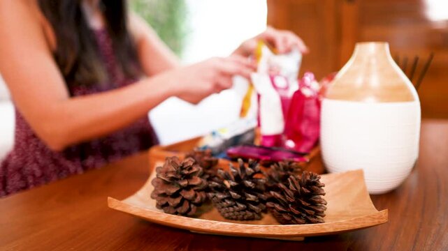 Asian Woman Arranging Essential Oil Diffuser and Pinecones on Wooden Table