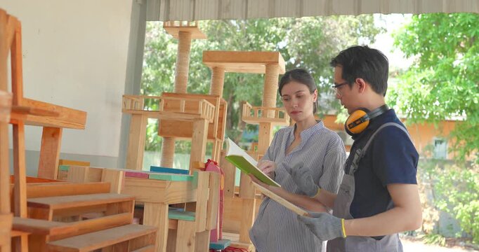 Entrepreneur and carpenter review wooden furniture mockup and prototype pieces, discuss design details and inspect quality at a small business workshop during product development.
