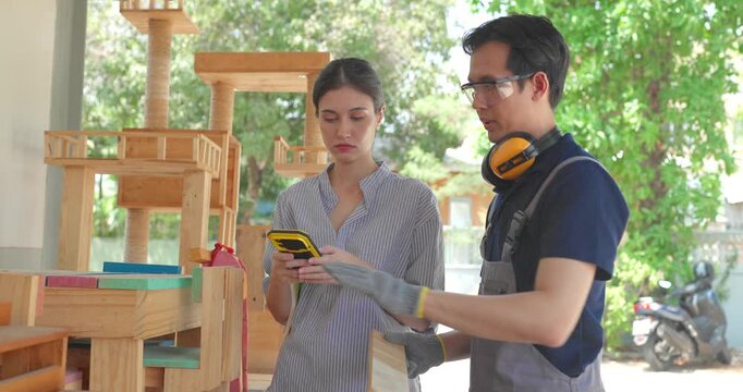 Entrepreneur and carpenter review wooden furniture mockup and prototype pieces, discuss design details and inspect quality at a small business workshop during product development.
