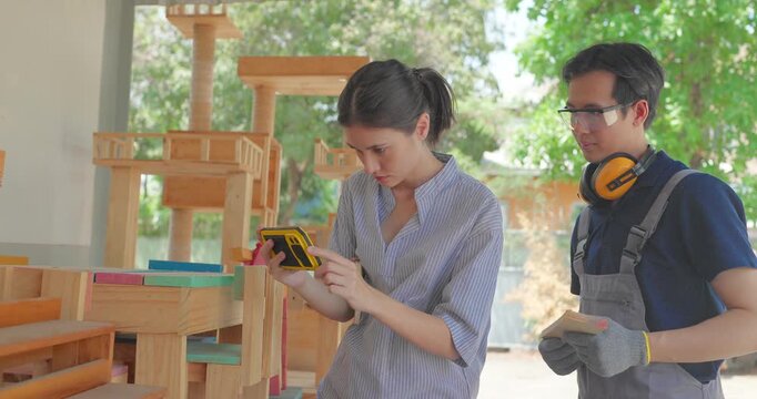 Entrepreneur and carpenter review wooden furniture mockup and prototype pieces, discuss design details and inspect quality at a small business workshop during product development.
