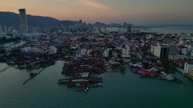 historic wooden clan jetties and waterfront homes contrasting modern skyline and hills in George Town, Penang, Malaysia. Amazing aerial view panorama orbit overview drone