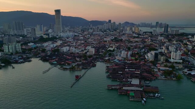 historic wooden clan jetties and waterfront homes contrasting modern skyline and hills in George Town, Penang, Malaysia. Dramatic aerial view drone shot panorama from above
