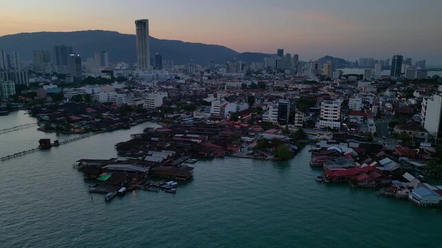 historic wooden clan jetties and waterfront homes contrasting modern skyline and hills in George Town, Penang, Malaysia. Beautiful aerial view fly push forward panorama drone