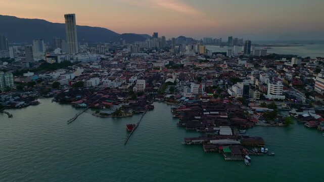 historic wooden clan jetties and waterfront homes contrasting modern skyline and hills in George Town, Penang, Malaysia. Unique aerial view rotation pan to right panorama drone