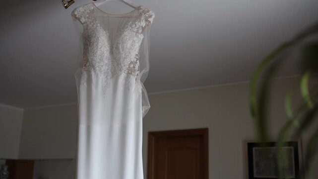 White wedding dress with lace bodice hanging on hanger indoors showing full length garment ready for ceremony
