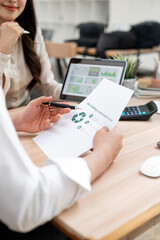 Plakat Businesswoman holding document with recycle icon and analyzing ESG data on tablet in office, sustainable business concept.