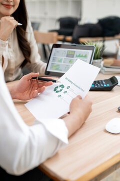 Businesswoman holding document with recycle icon and analyzing ESG data on tablet in office, sustainable business concept.
