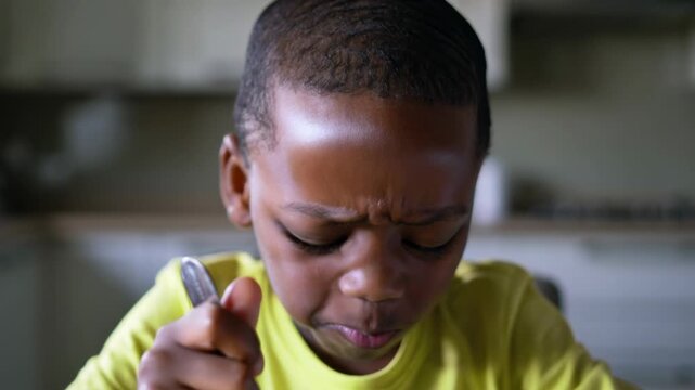 An African American boy eats porridge, expressing dissatisfaction. He has no appetite