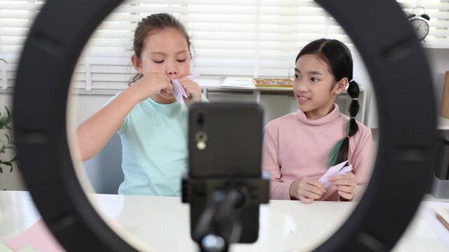 Modern young students online learning content creator, elementary girls explain homework to teacher record paper activity by phone, digital education, creativity vlog, alpha generation study children