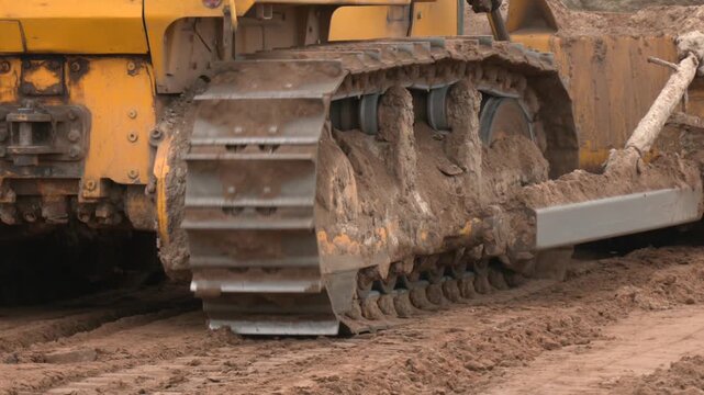 Construction tractor with specialized dozer blade pushing and grading soil at excavation site. Heavy machinery transforming raw land into prepared foundation for upcoming building development project
