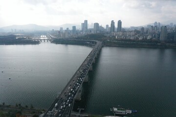 Naklejka premium Aerial shot of a long bridge crossing a wide river with city skyline in the background.