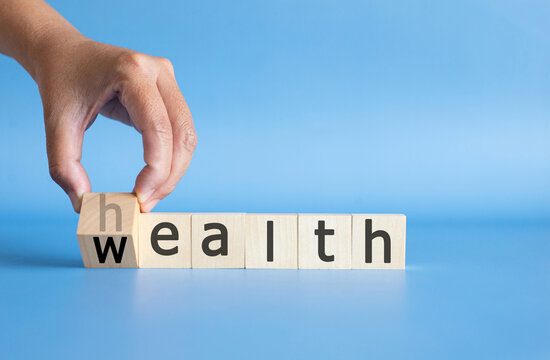 Hand turning wooden cubes from health to wealth word on blue background