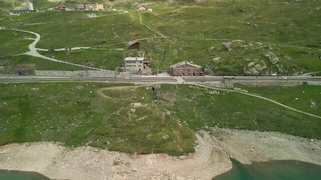 Stunning aerial footage of remote alpine buildings beside the elevated Grimsel Pass road. Captures rugged terrain and tranquil mountain scenery under natural daylight, showcasing Switzerland's breatht