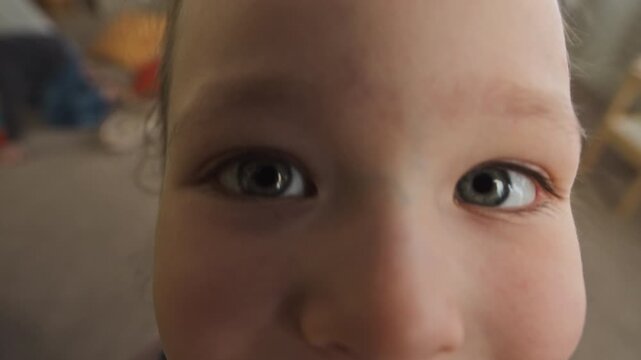High angle POV slowmo shot of adorable Caucasian girl with blue eyes smiling while looking at camera with curiosity