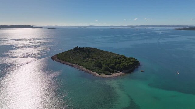 Drone over Veli &Scaron;kolj and a nearby islet with sun shimmering on the Adriatic. The camera turns to reveal turquoise shallows, Pako&scaron;tane town, and Vrana Lake stretching behind.