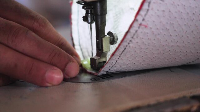 Close-up of a sewing machine stitching fabric for a traditional songkok in Malaysia. Skilled craftsmanship and precise hand guidance highlight cultural garment production and artisanal work.